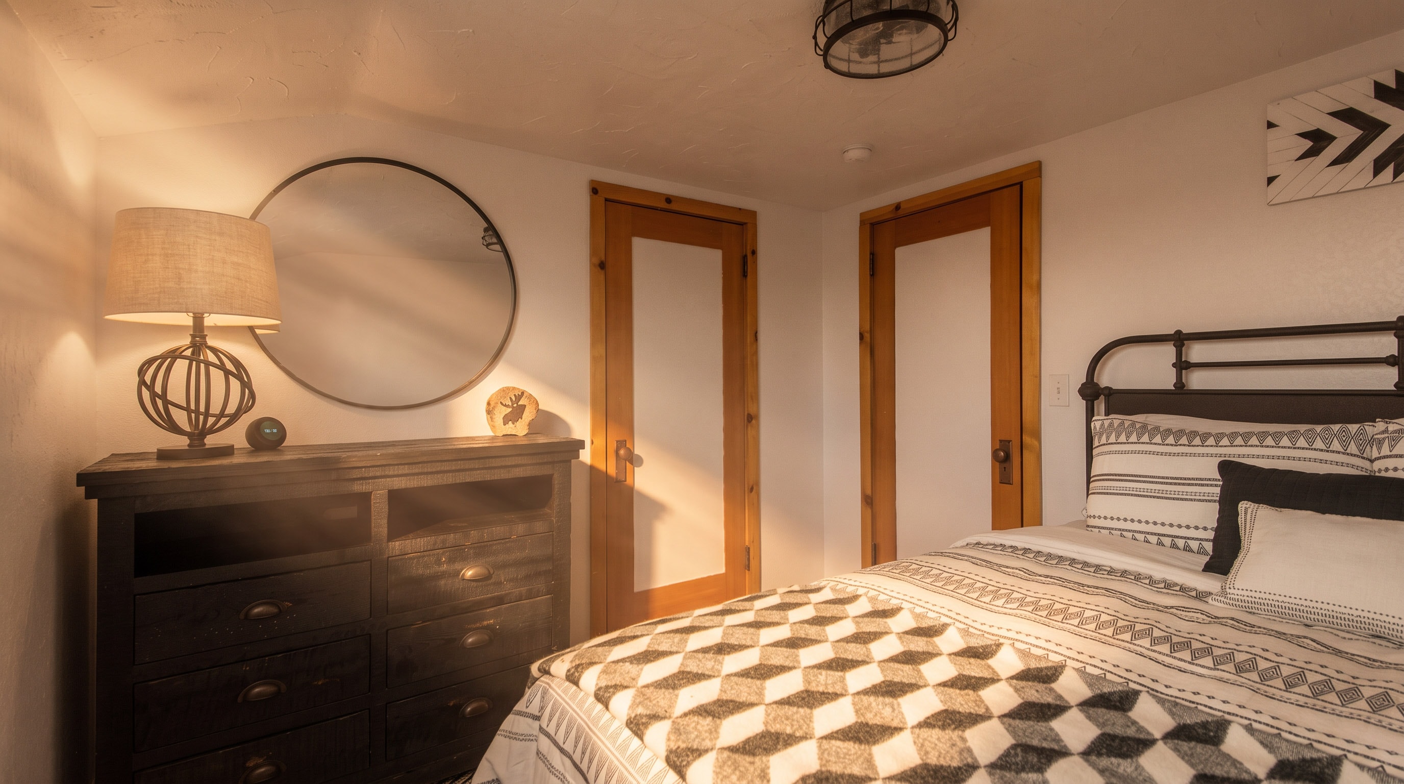 Upstairs Bedroom 2 — iron bed frame with geometric bedding and round mirror