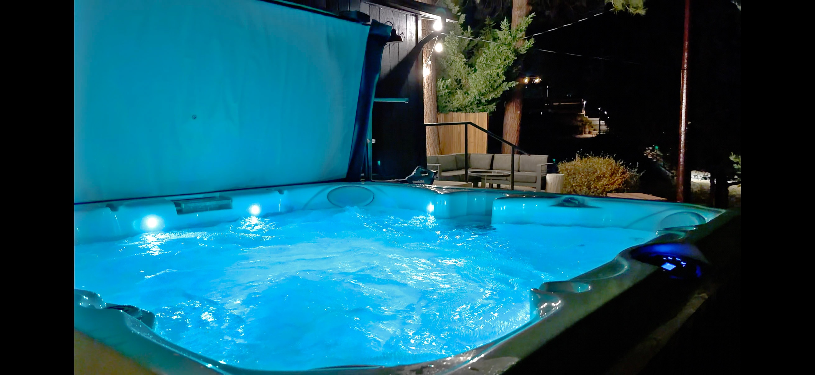 Hot tub close-up at night with blue LED lighting and outdoor seating beyond