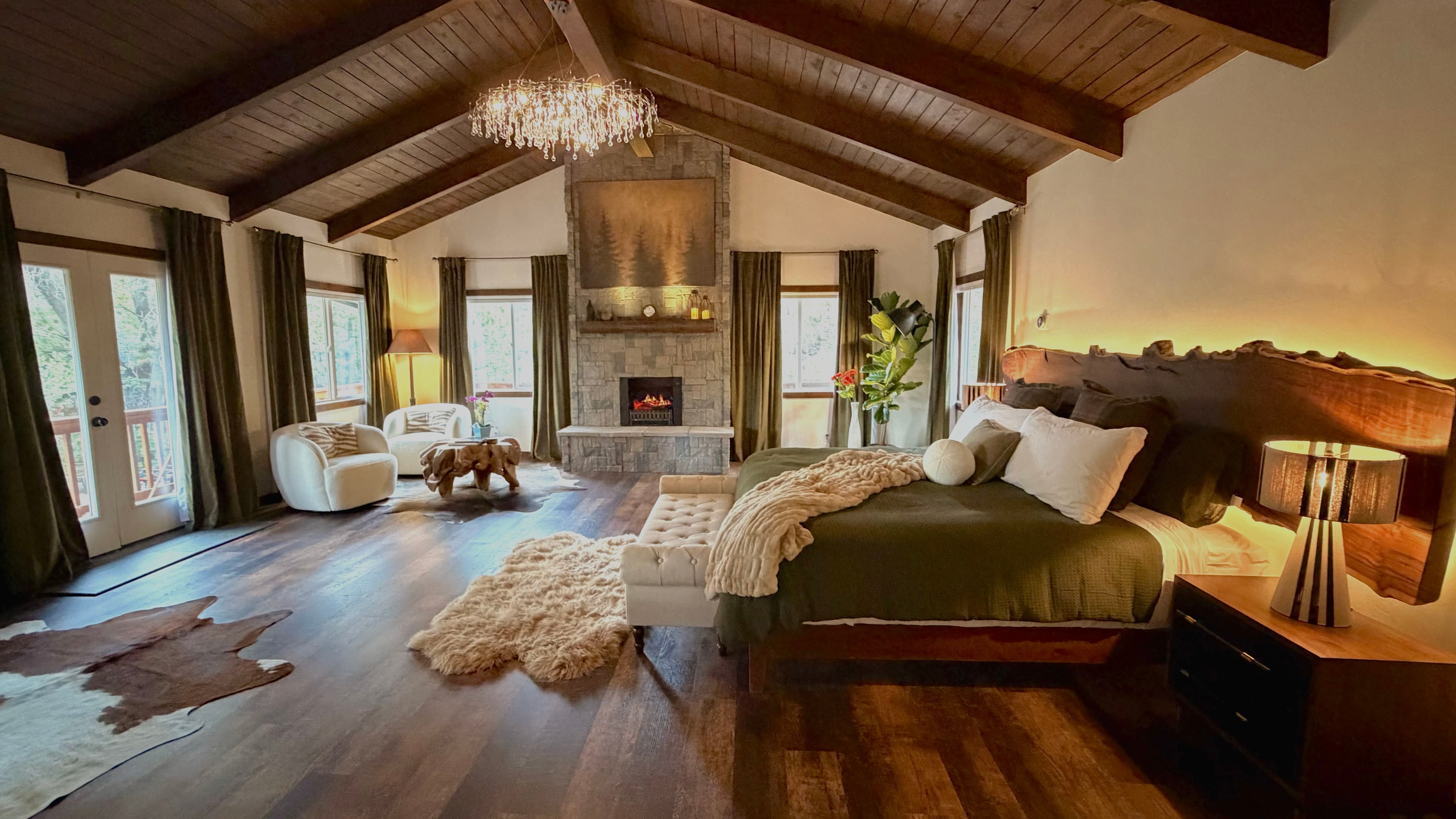 Master Suite — vaulted ceiling with timber beams, crystal chandelier, stone fireplace, and king bed with live-edge headboard