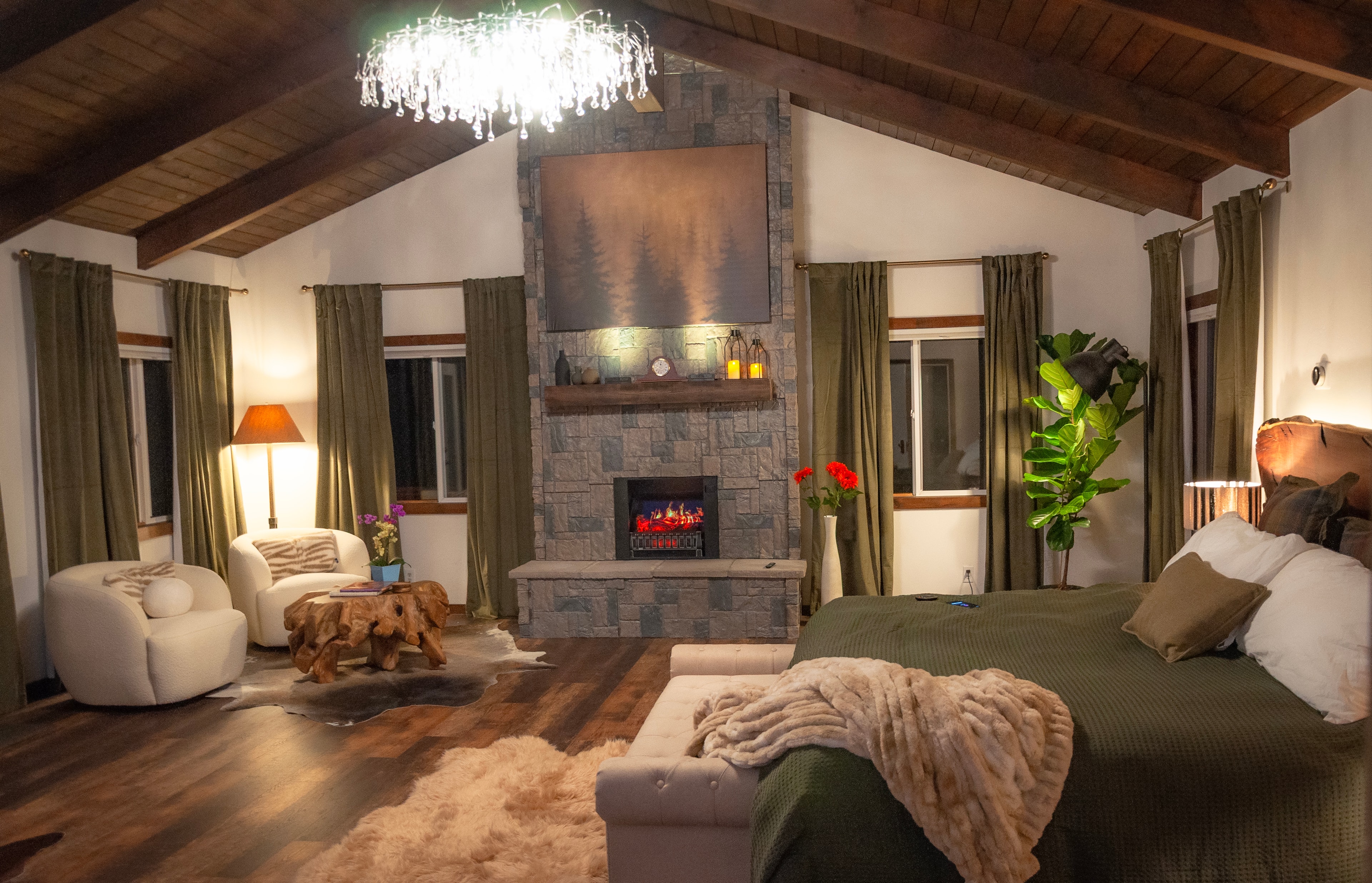 Master Suite — evening view of stone fireplace, sitting area, and king bed with forest views
